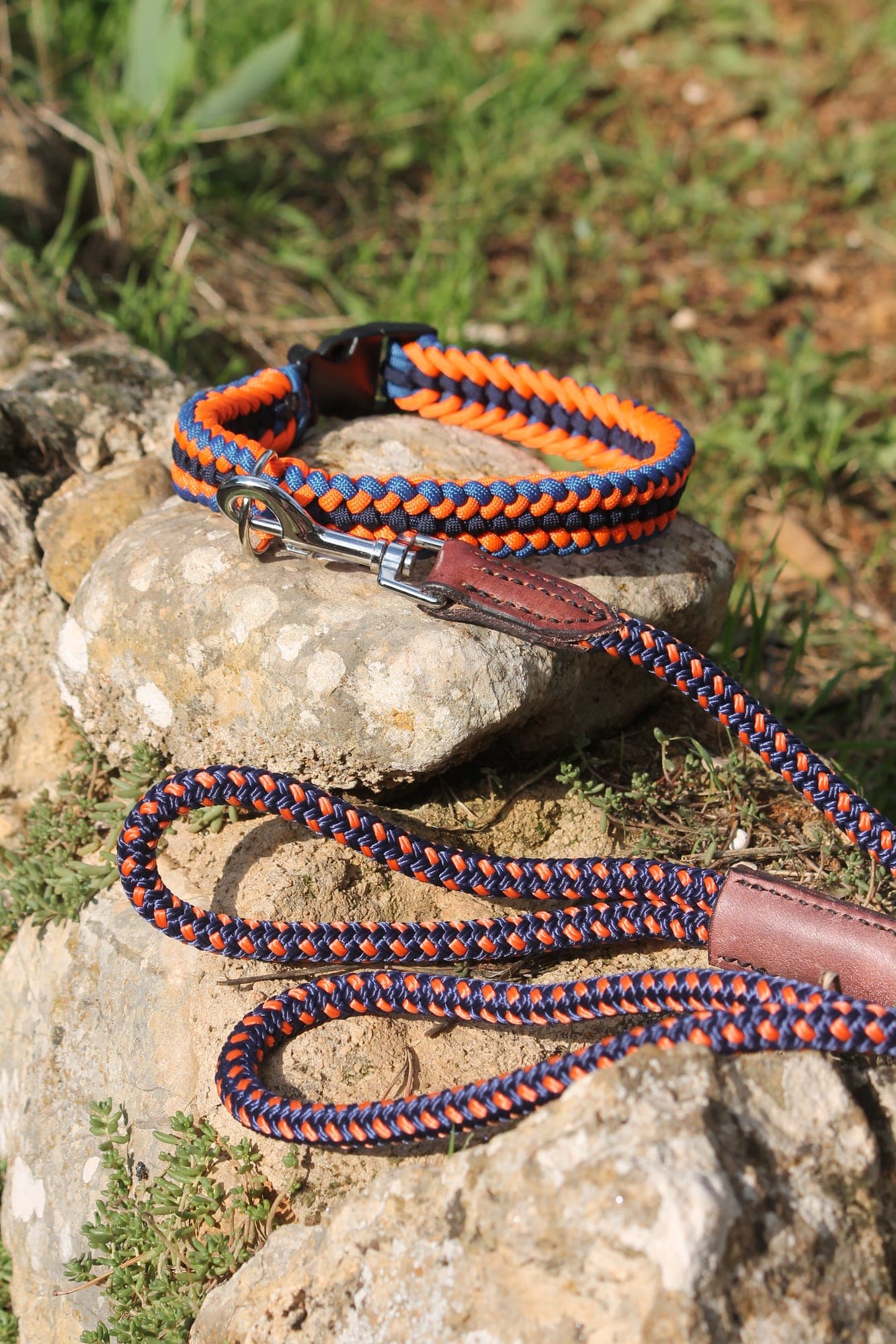 Collier en paracorde tressée bleu marine et orange avec sa laisse assortie à poignée de cuir, posés sur un rocher.