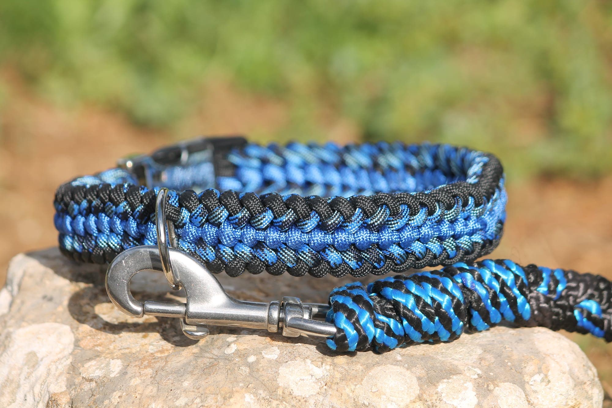 Collier en paracorde tressée noire et bleue, mousqueton inox et laisse assortie, posés sur une pierre.